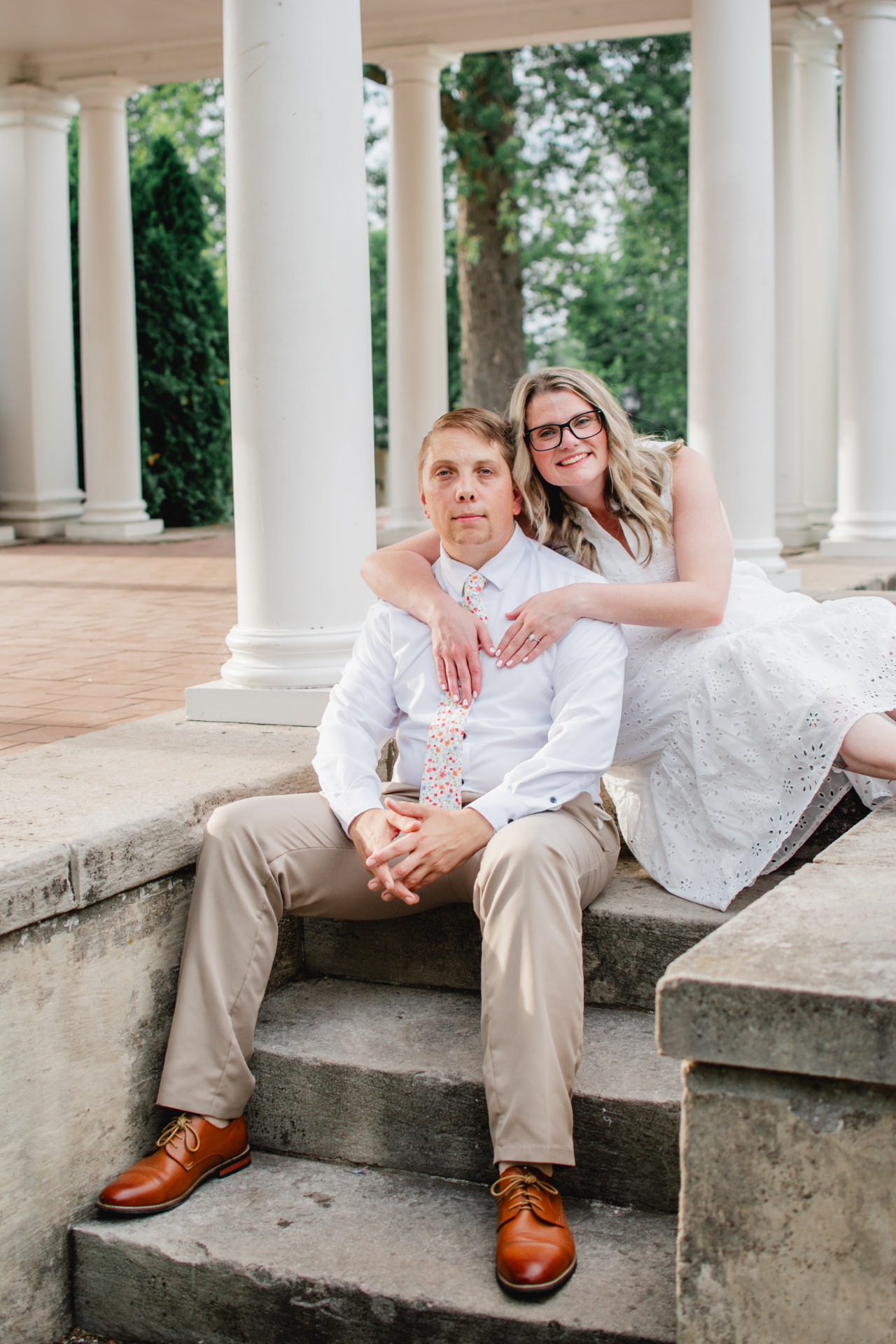 Engaged couple seated on stone steps between white columns